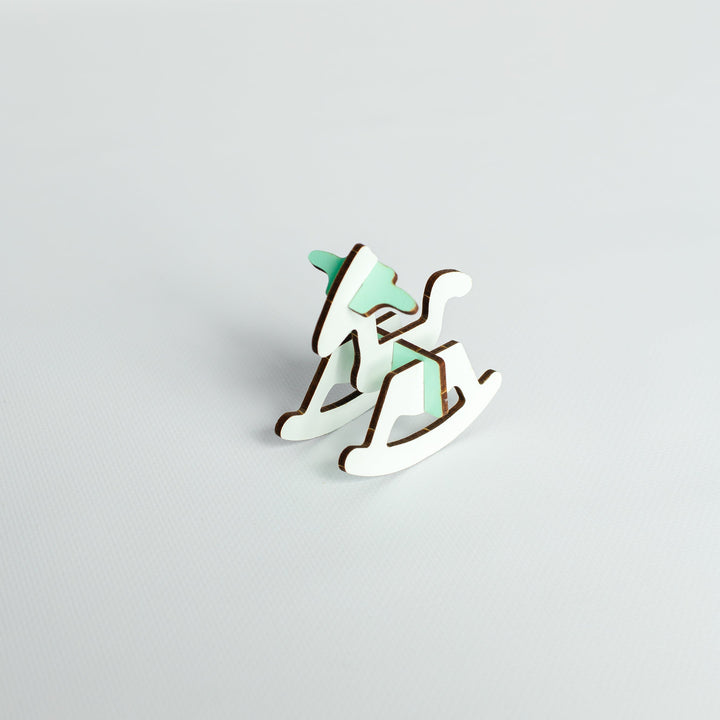 A small wooden rocking horse figurine with a mint green painted finish and natural brown wood edges, set against a plain light gray background.