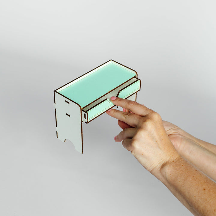 A hand holding a small mint green and white laser-cut wooden box against a plain light gray background.