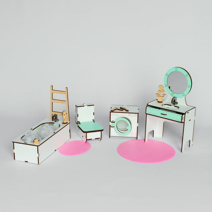 A miniature dollhouse-style bathroom furniture set with a bathtub, ladder, chair, washing machine, vanity table, mirror, and pink circular rugs on a light gray background.