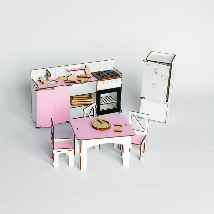 A miniature dollhouse kitchen and dining set, featuring a pink and white kitchen with a stove, oven, and refrigerator, alongside a matching pink and white dining table with chairs.