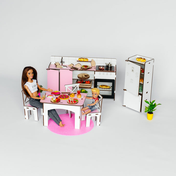 A dollhouse miniature kitchen set with a pink and white refrigerator, stove, dining table, chairs, and a small potted plant, styled with tiny dolls on a white background.