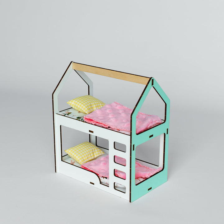 A miniature dollhouse-style bed frame with two bunk beds, decorated with pink bedding and yellow pillows, set against a plain light gray background.