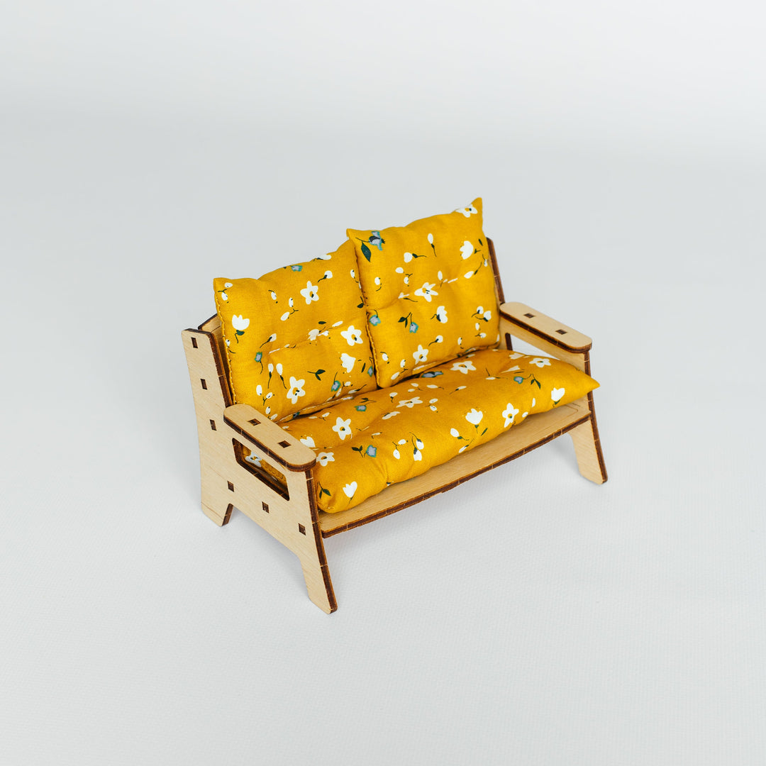 A miniature wooden loveseat with mustard yellow floral cushions, photographed on a seamless light gray studio background.