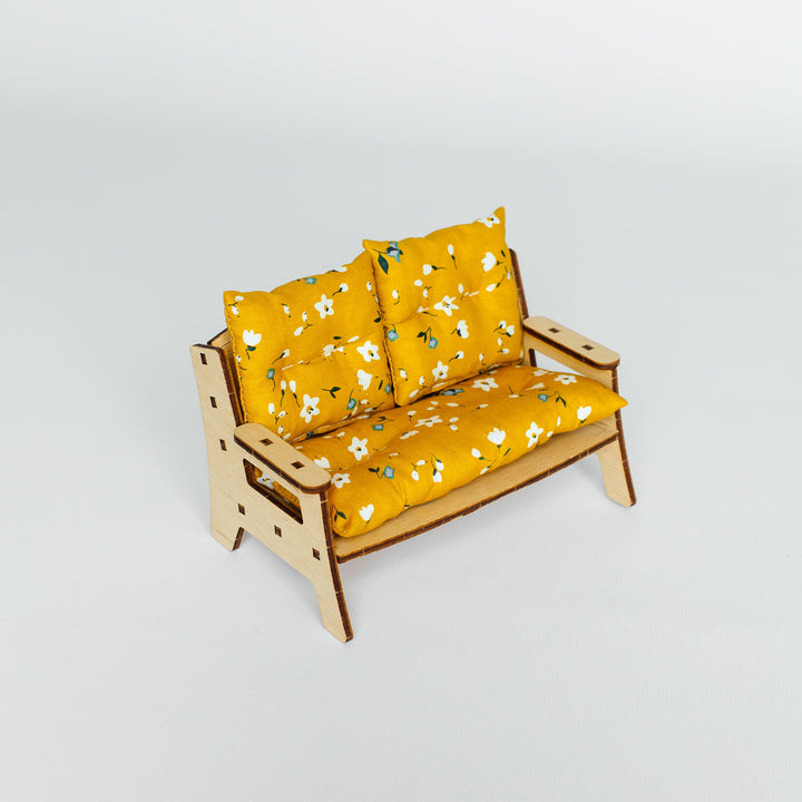 A miniature wooden loveseat with mustard yellow floral cushions, photographed on a seamless light gray studio background.
