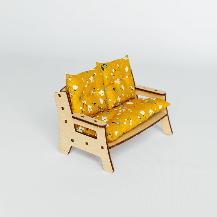 A miniature wooden loveseat with yellow floral cushions, photographed on a seamless light gray studio background.