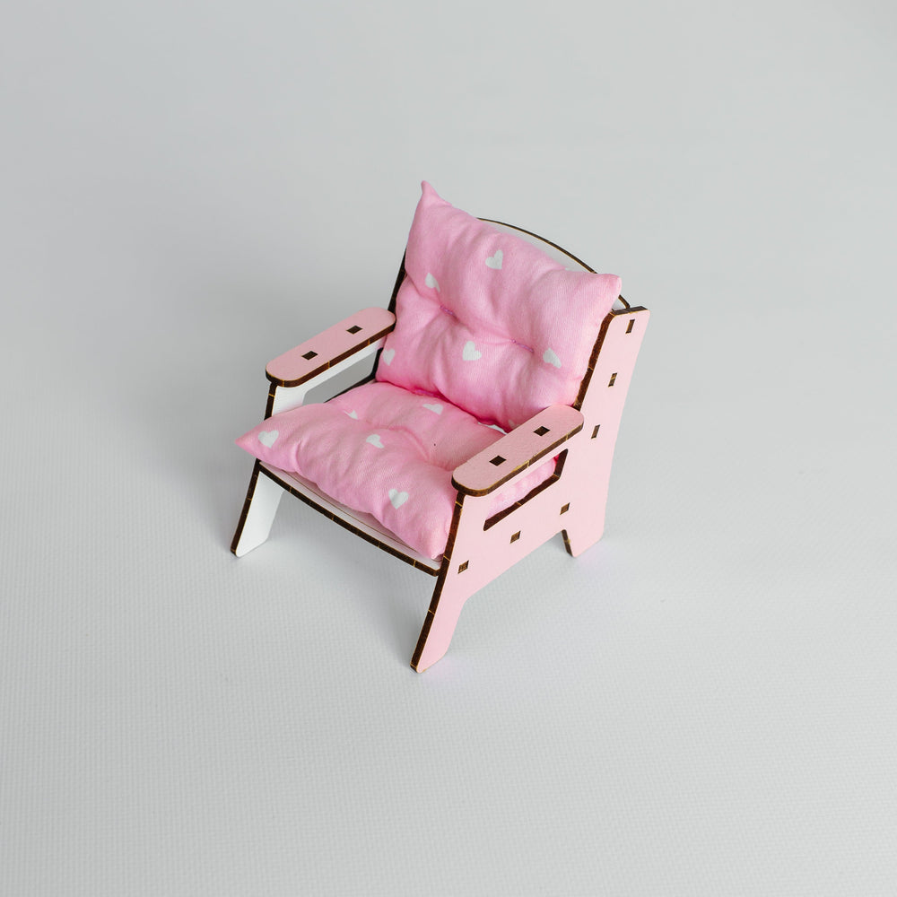 A miniature pink doll chair with a matching pink cushion, featuring a light wood frame and small white feet, set against a plain light gray background.