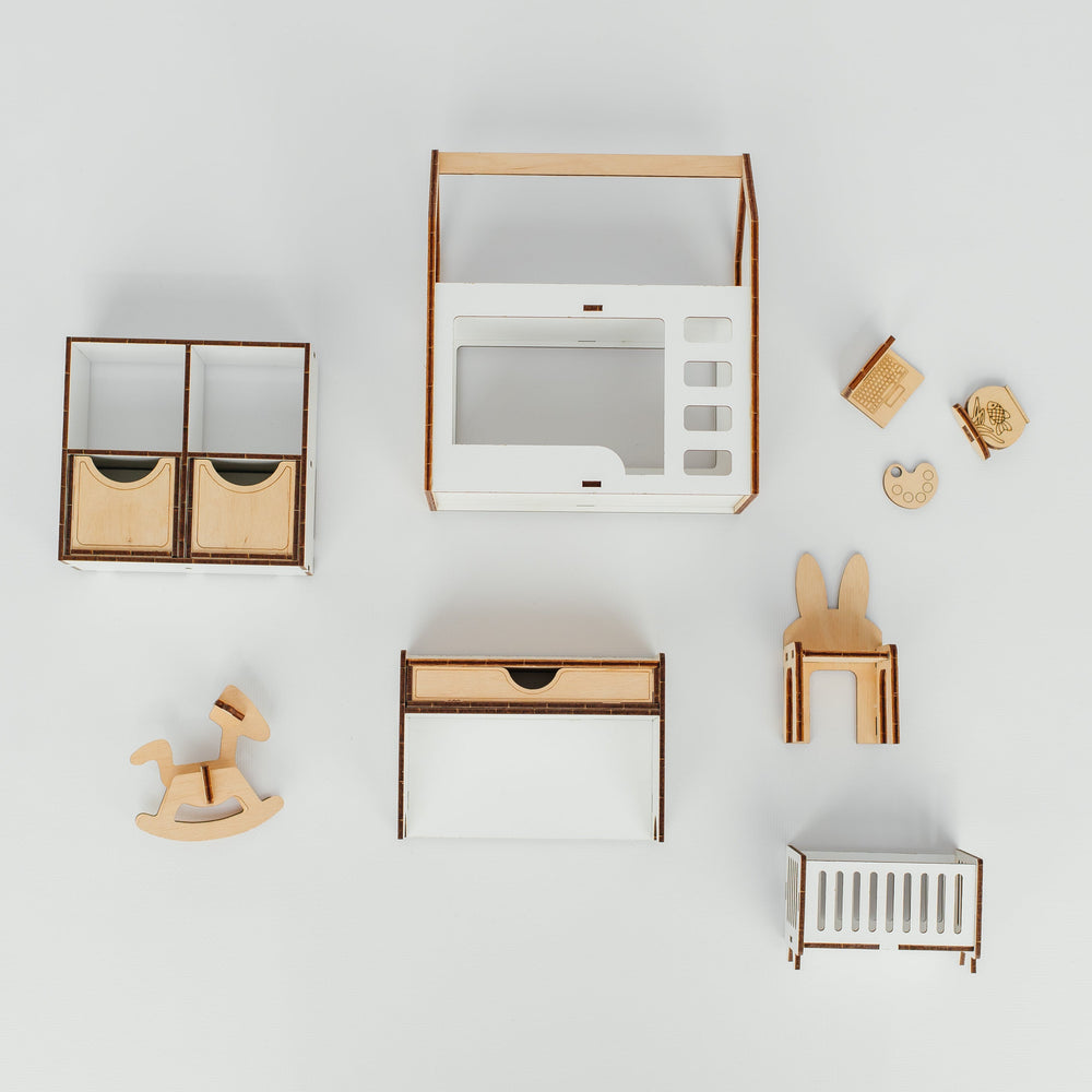 A top-down view of a children's wooden play kitchen and matching accessories arranged on a light gray background. The set includes a play kitchen with a white body and natural wood trim, a small cabinet, a rocking horse, a chair, a bunny-shaped stool, a crib, and small wooden toy pieces.