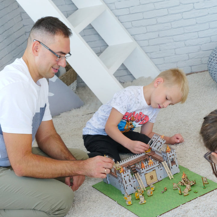 Man and two children playing with a toy house on the floor.