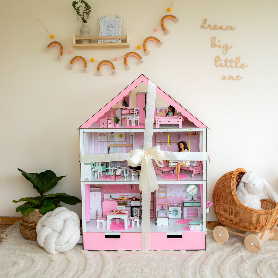 Pink dollhouse with toys inside, surrounded by decorative items on a light-colored floor.