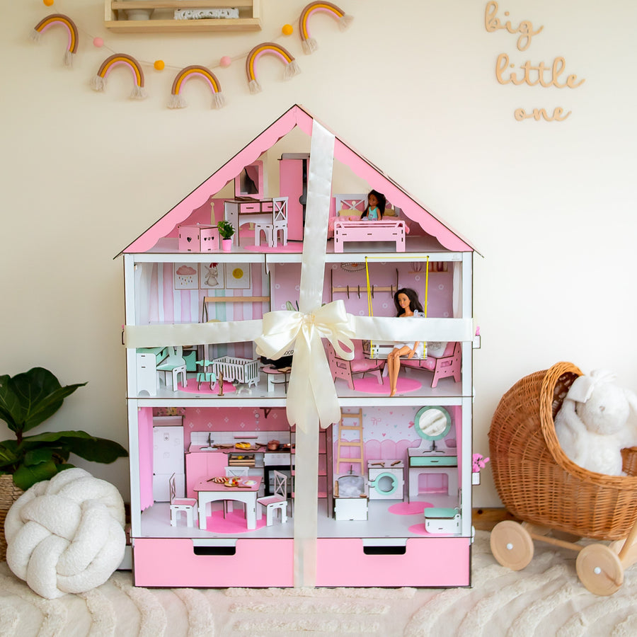 Pink dollhouse with toys inside, surrounded by decorative items on a light-colored floor.