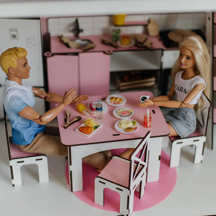 Two dolls, a boy and a girl, sitting at a pink dining table with food and drinks.