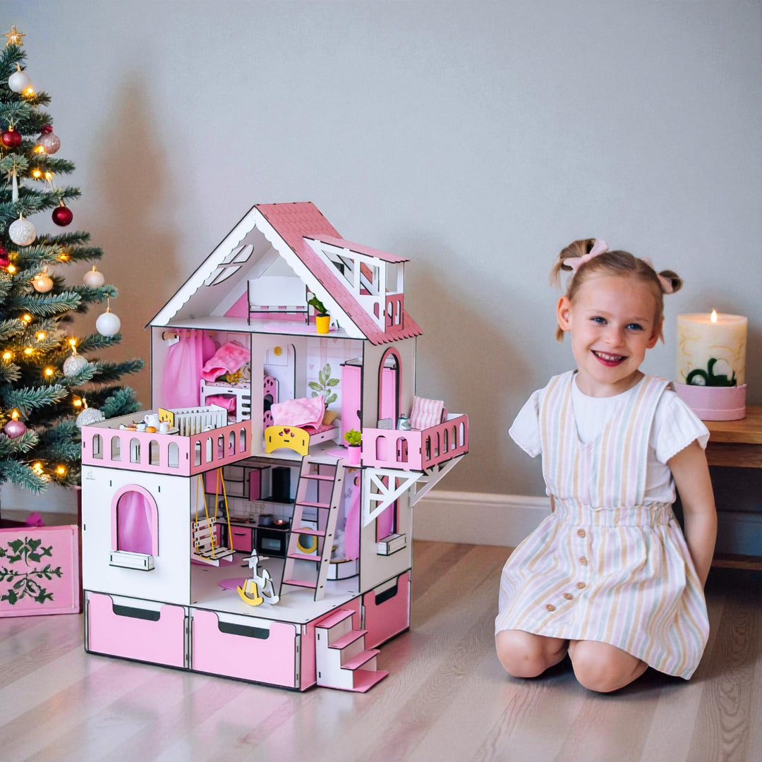 Young girl posing with a pink dollhouse in a room decorated for Christmas.