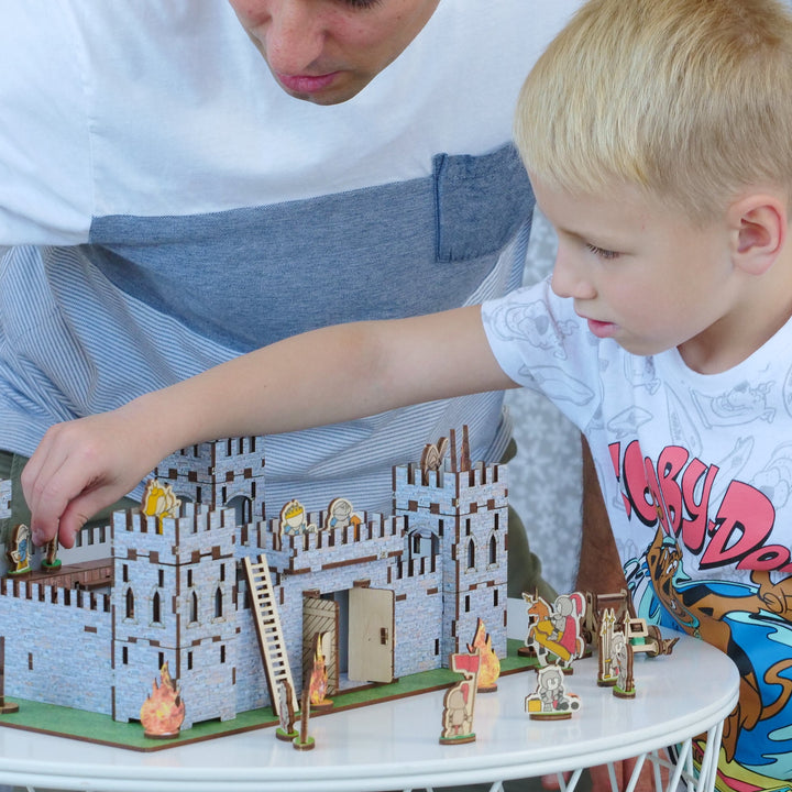 Two children playing with a model castle on a small table.