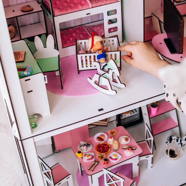 Dollhouse with a person playing with a toy figure on a pink bed.