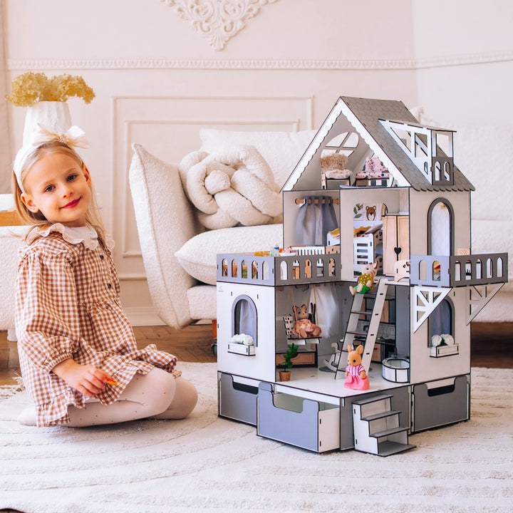 A wooden dollhouse mini cottage with an organizer scale 1:12, featuring a white and grey color scheme, with a young child sitting beside it.