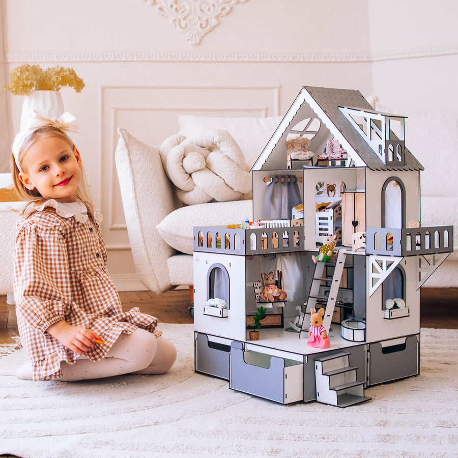 A wooden dollhouse mini cottage with an organizer scale 1:12, featuring a white and grey color scheme, with a young child sitting beside it.